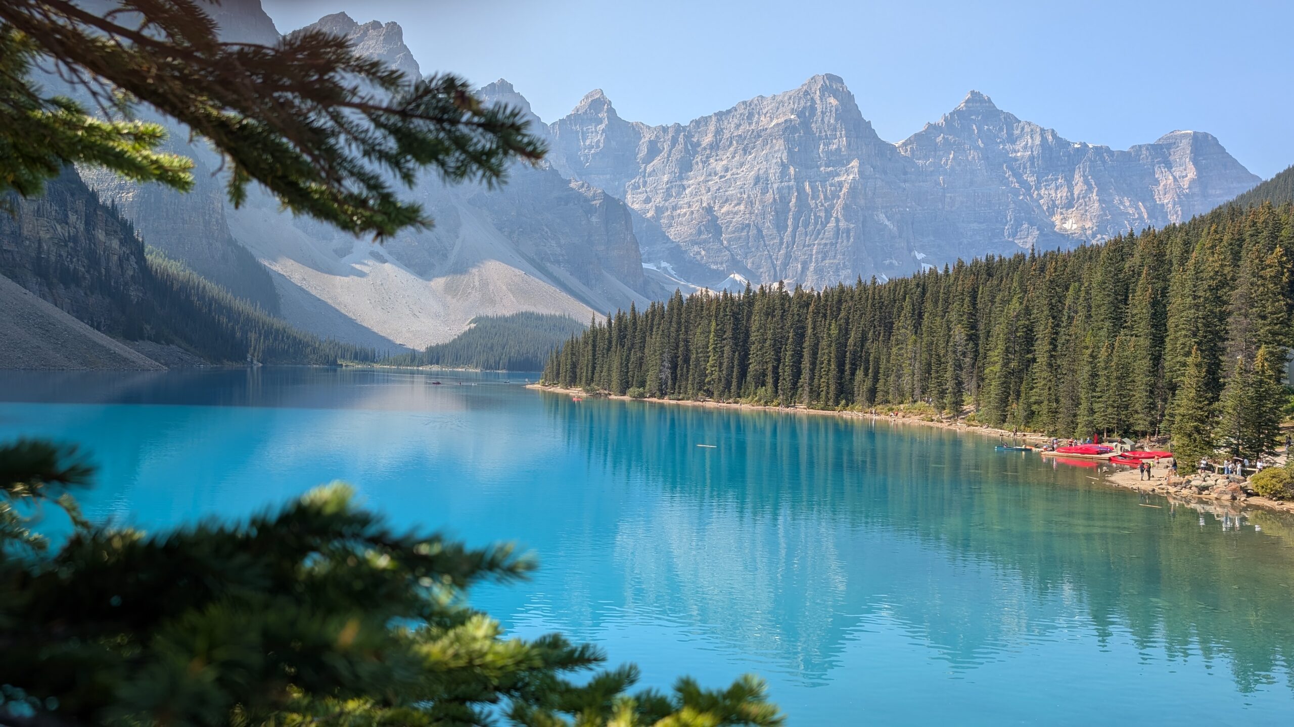 Wide panoramic view of Moraine Lake in early September, with turquoise water, surrounding peaks of the Valley of the Ten Peaks, and autumn colors beginning to appear