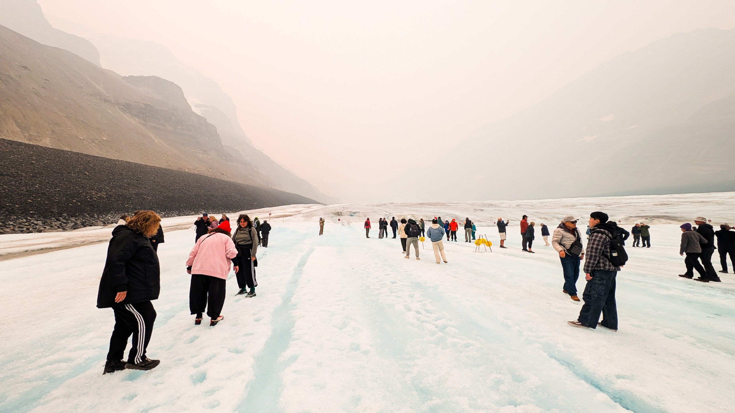 Visitors standing on the Columbia Icefield taking photos with the Athabasca Glacier and surrounding mountains