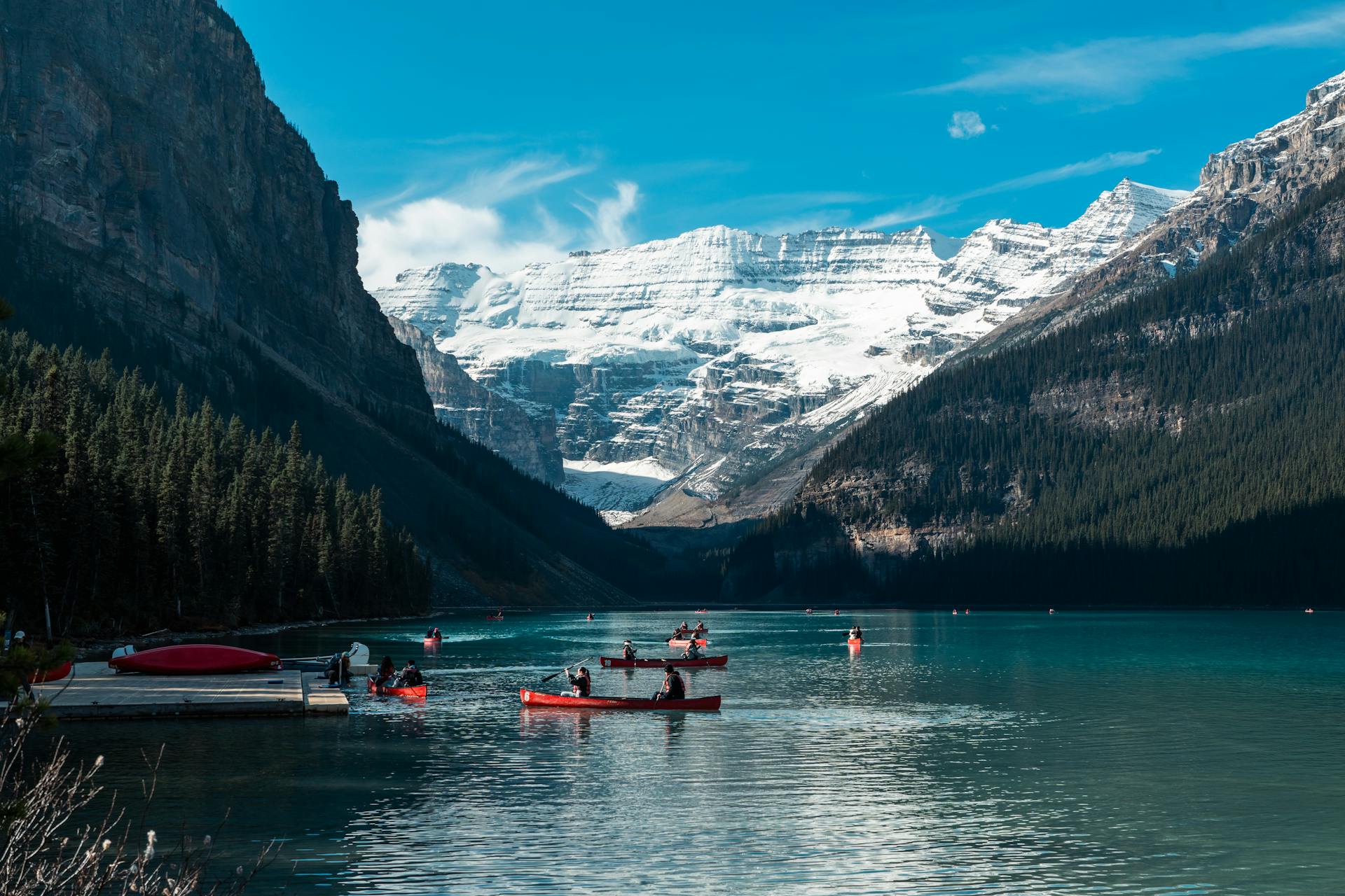 People canoeing on turquoise Lake Louise in summer, surrounded by mountain peaks and glaciers in Banff National Park