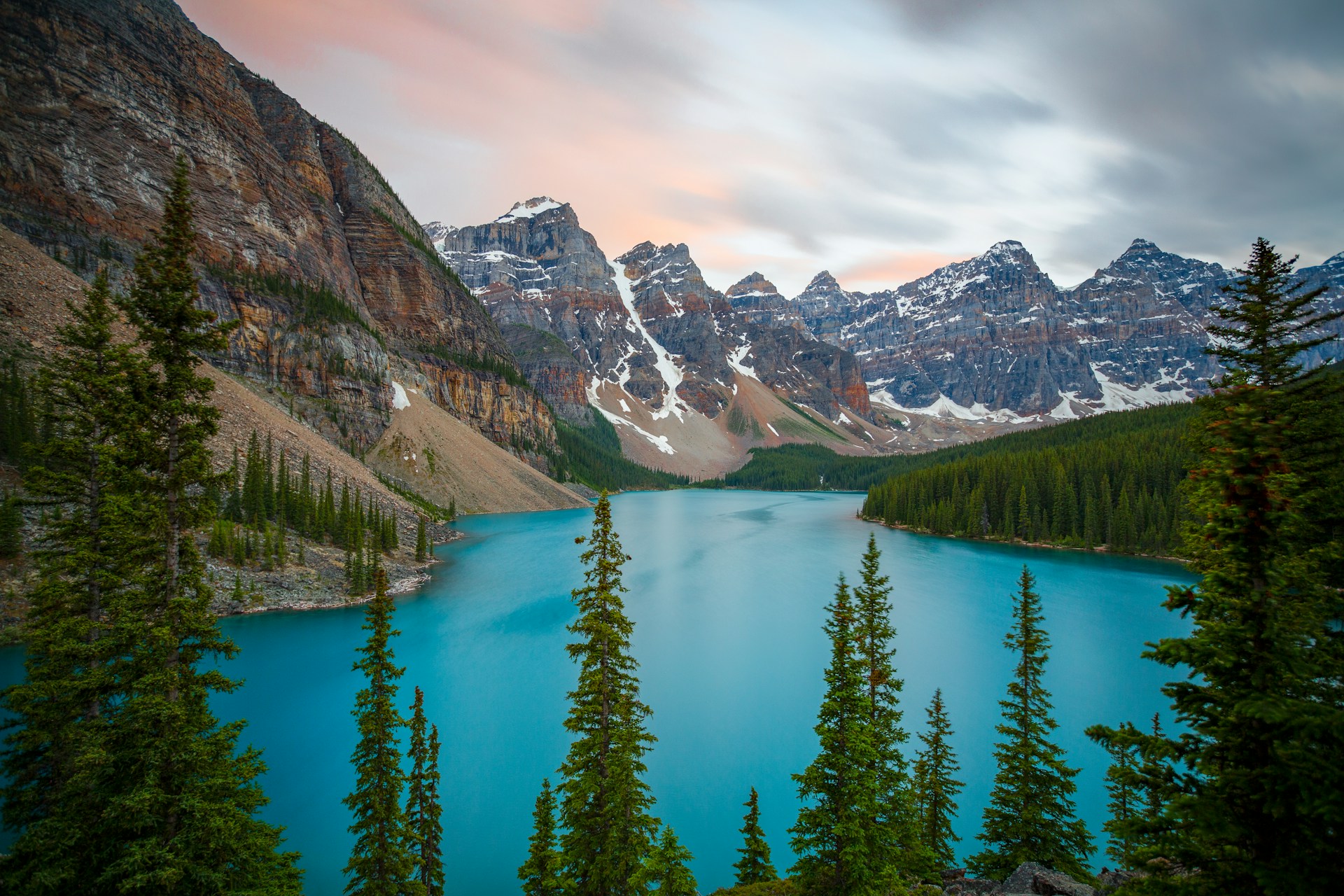 Moraine Lake in spring with visible glaciers, lingering snow on surrounding peaks, and partially thawed water in Banff National Park