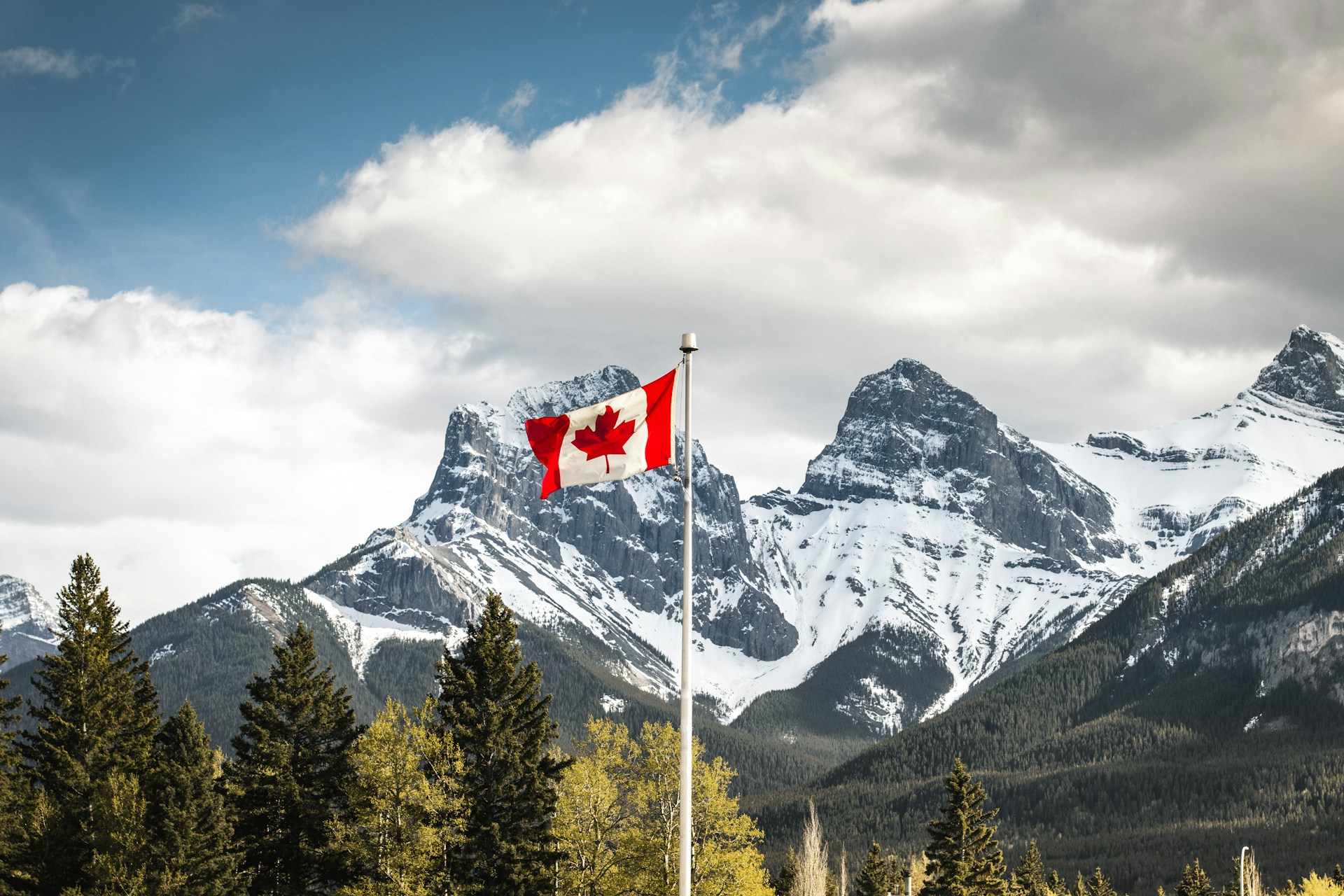 A Canadian flag flying in front of the Three Sisters peaks above Canmore, Alberta