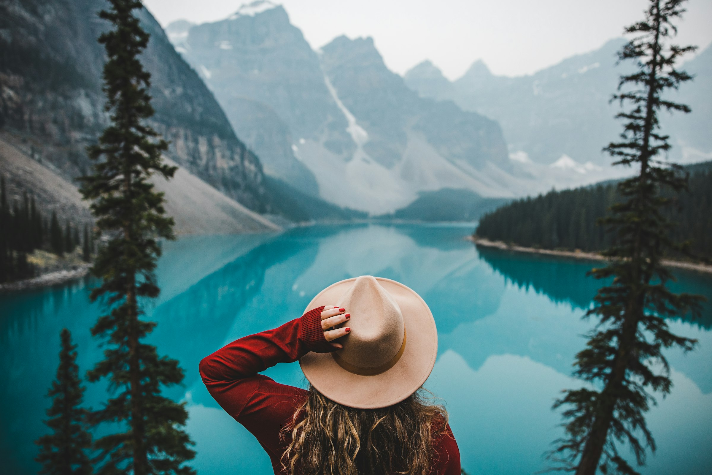 A woman in a wide-brim hat looking out over Moraine Lake's turquoise water toward the Valley of the Ten Peaks