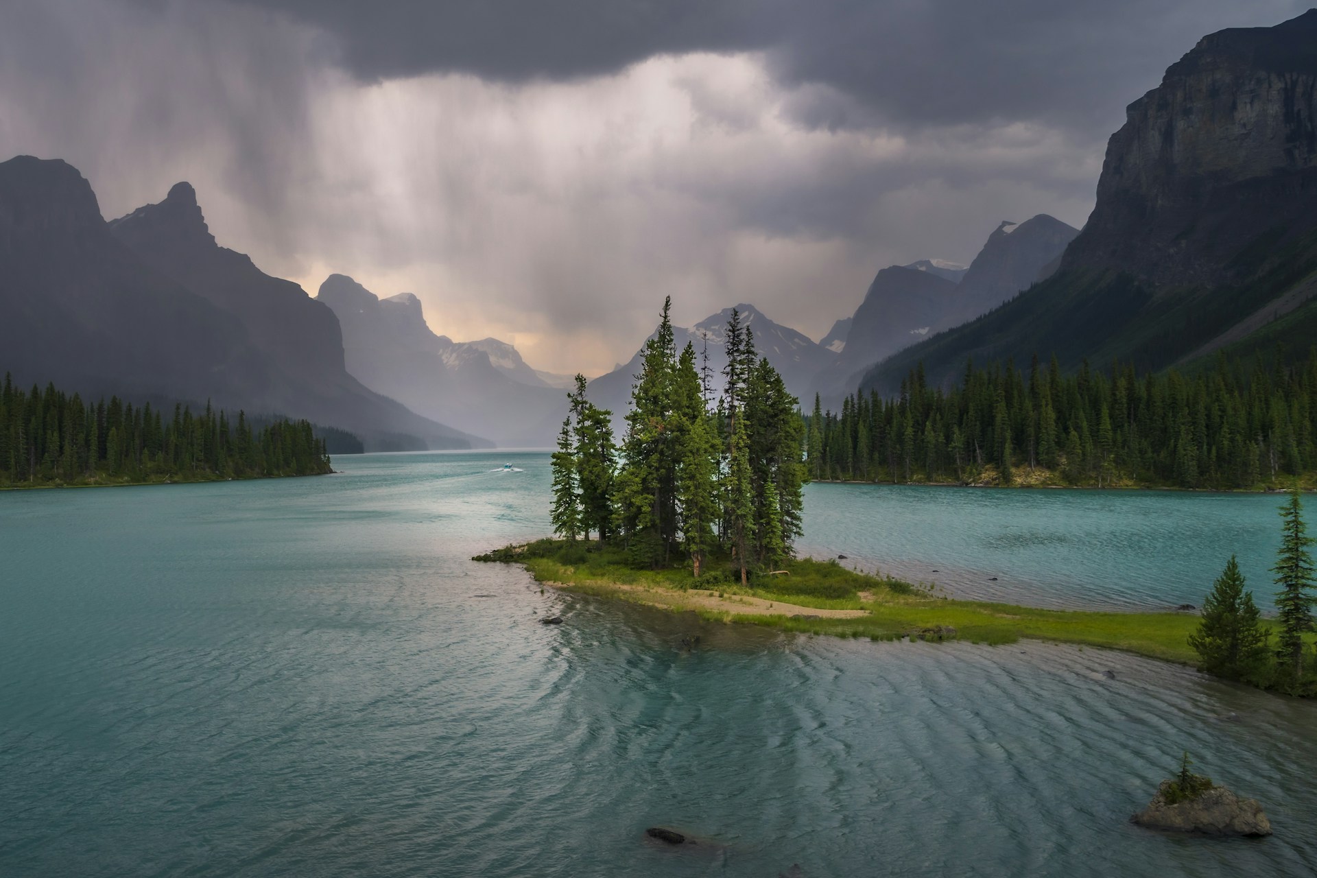 Spirit Island's pines under a dark storm sky on Maligne Lake, rain falling over the peaks at the far end of the lake