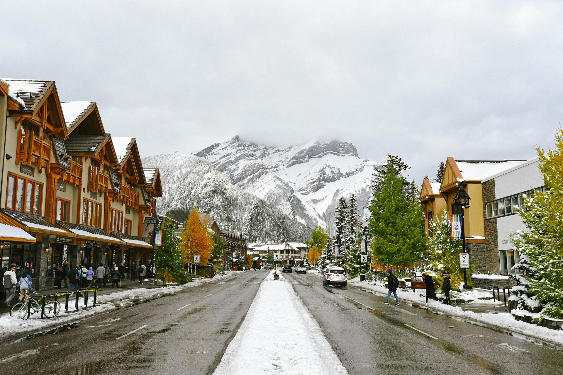 Banff Avenue after a fresh snowfall, with shops and people on the sidewalks and snow-covered Cascade Mountain rising at the end of the street