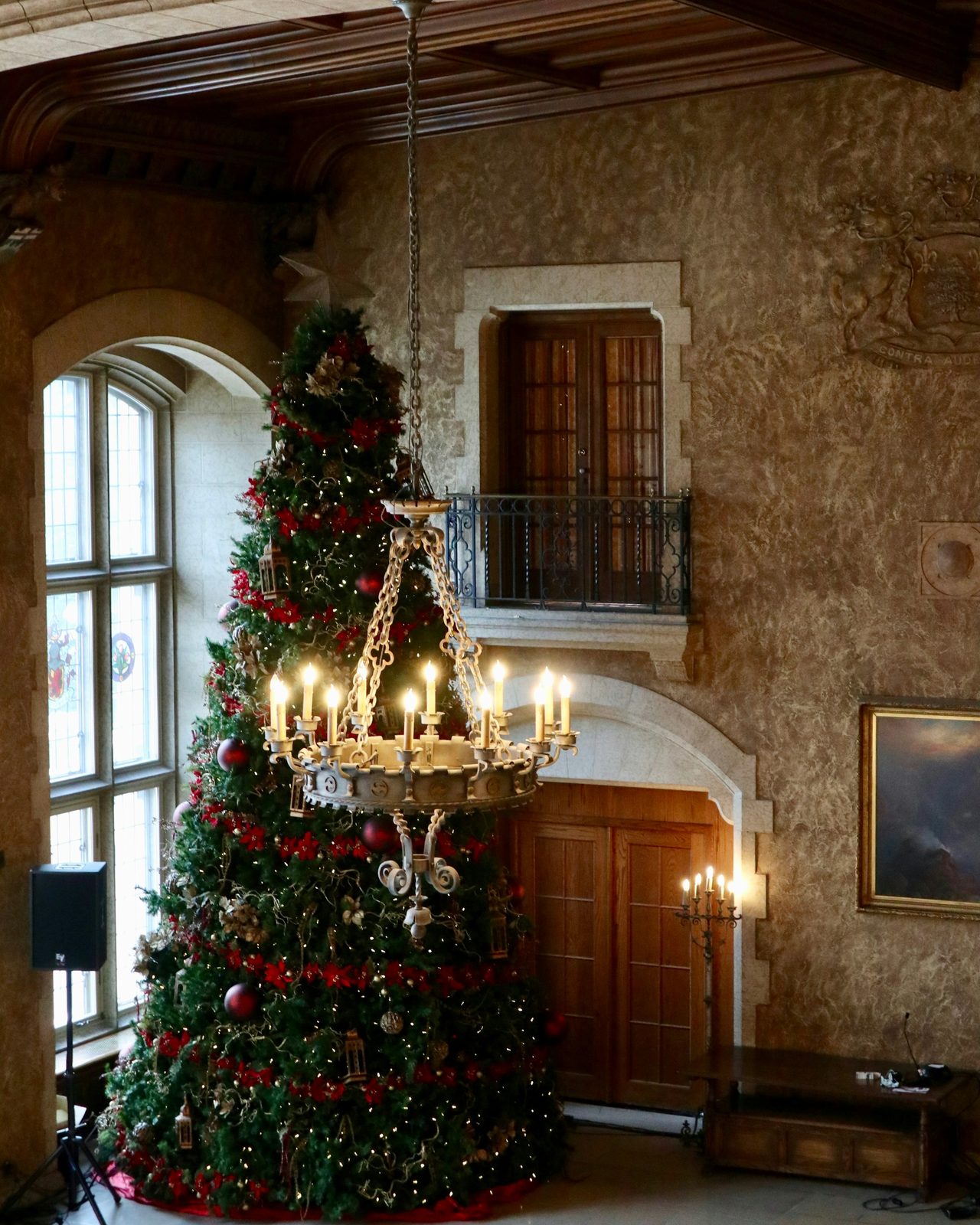 A tall decorated Christmas tree beside a candle chandelier in the stone-walled hall of a heritage hotel in Banff
