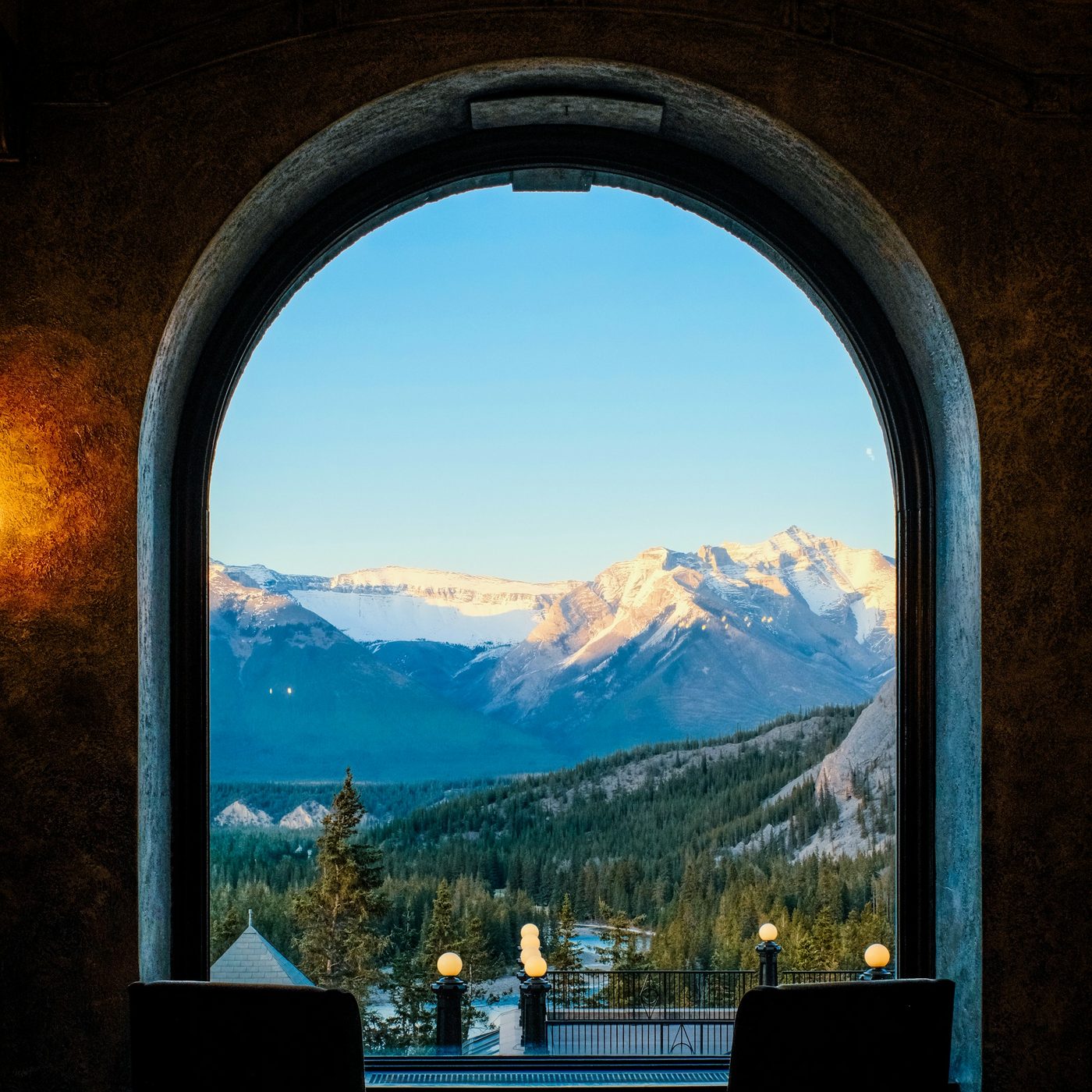 Snow-capped peaks and spruce forest seen through a tall arched window from inside a heritage hotel in Banff