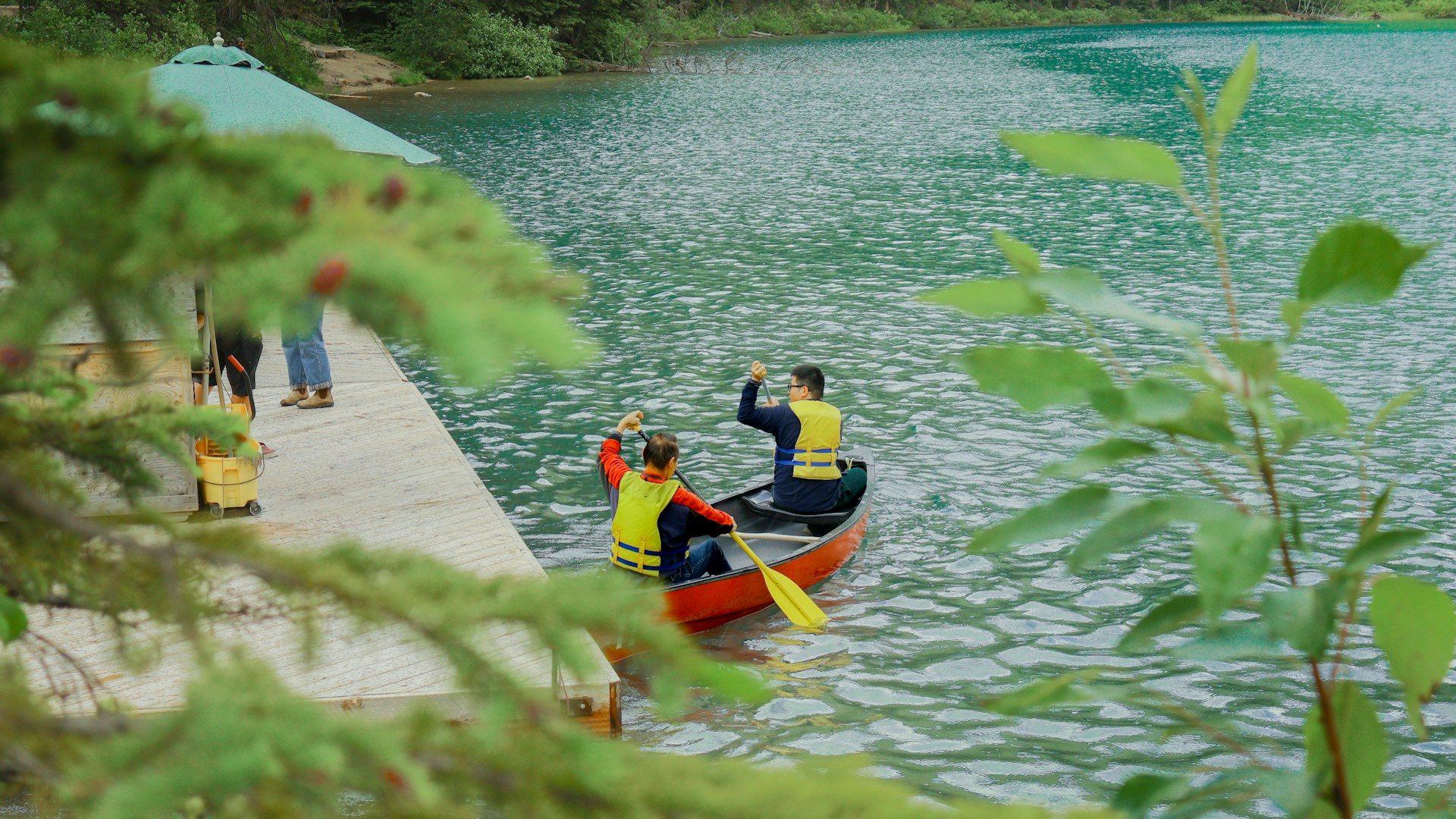 Two paddlers in yellow life jackets in a red canoe pulling away from the rental dock onto turquoise Emerald Lake