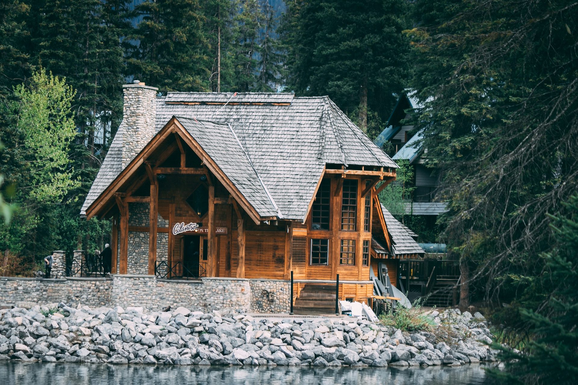 Close view of the timber-and-stone lakeside café building at Emerald Lake, with a stone chimney, cedar-shingle roof and a rock-lined shore