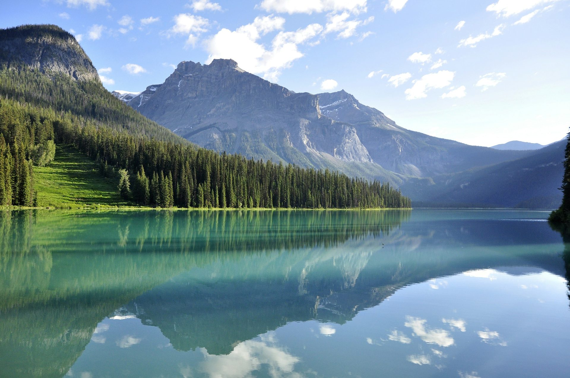 Calm Emerald Lake reflecting forested slopes, a mountain and white clouds on a clear day, Yoho National Park