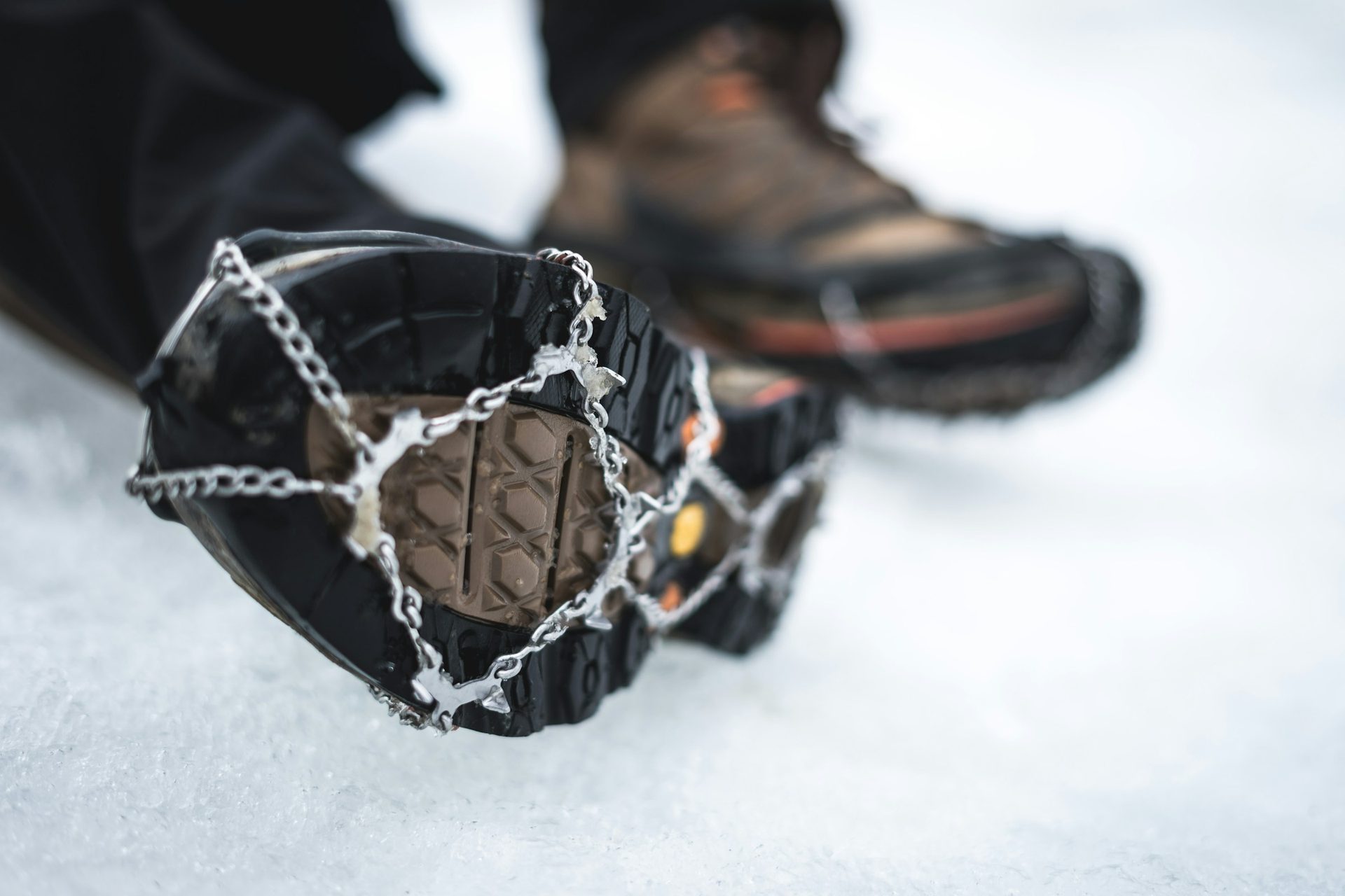 Close-up of a hiking boot fitted with chain-style ice cleats on packed snow