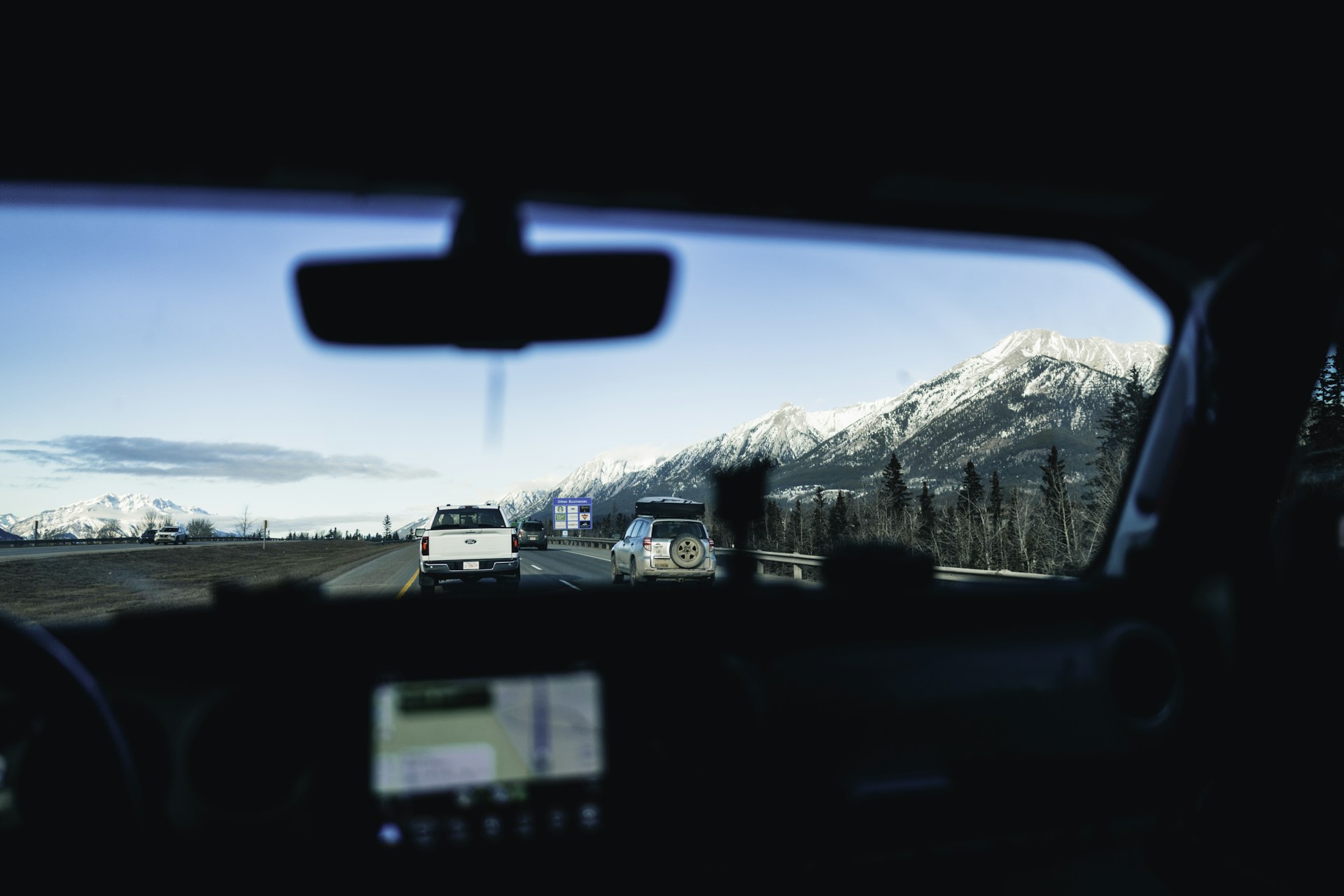 View through a car windshield of traffic on the divided Trans-Canada Highway near Canmore, with snow-capped peaks ahead